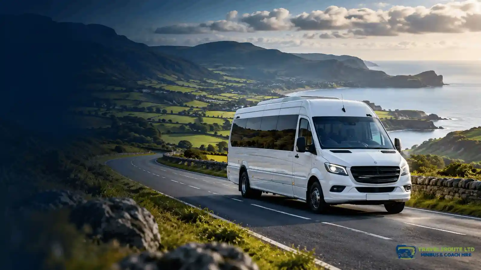 A TravelsRoute minibus on a coastal Welsh road through green hills and countryside