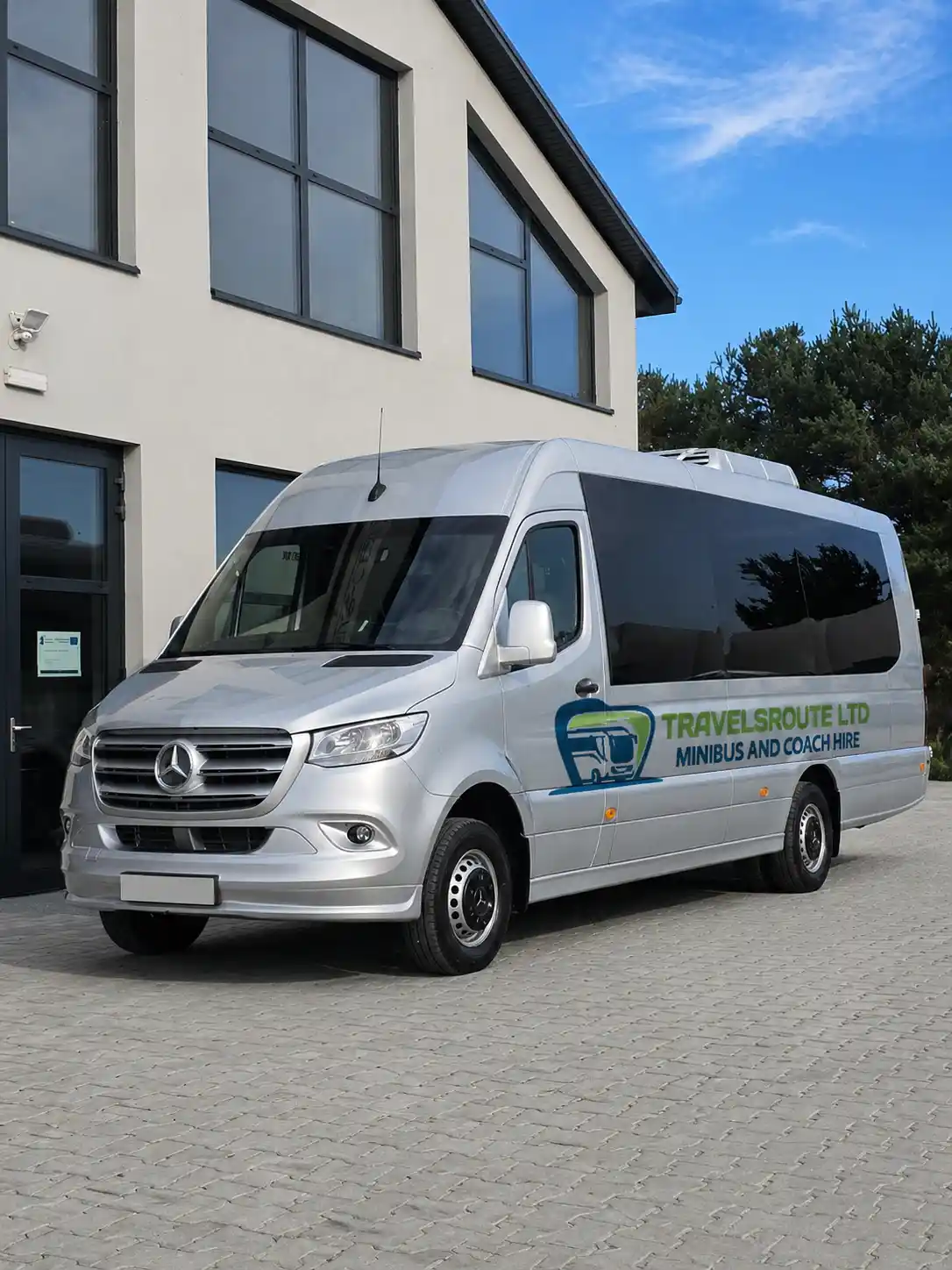 Silver minibus outside a modern glass building, like the studio and office blocks around MediaCityUK in Salford Quays
